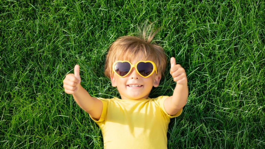 Little boy with thumbs up in grass with heart shaped sunglasses