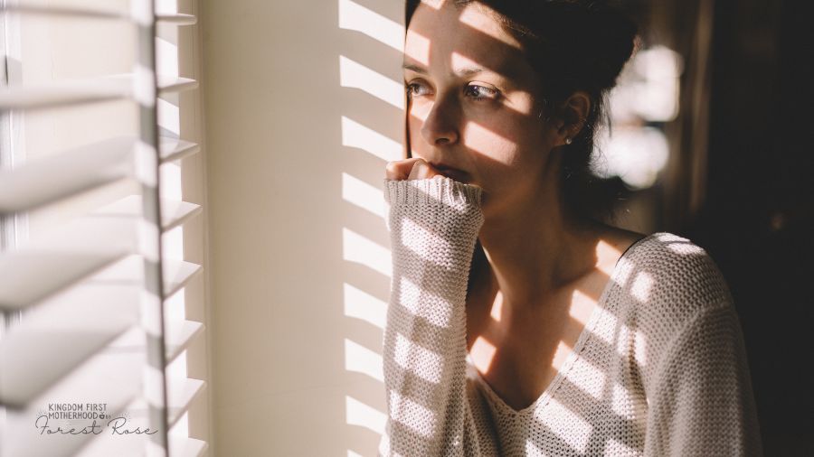 Sad or worried mom looking out the window shadow from blinds