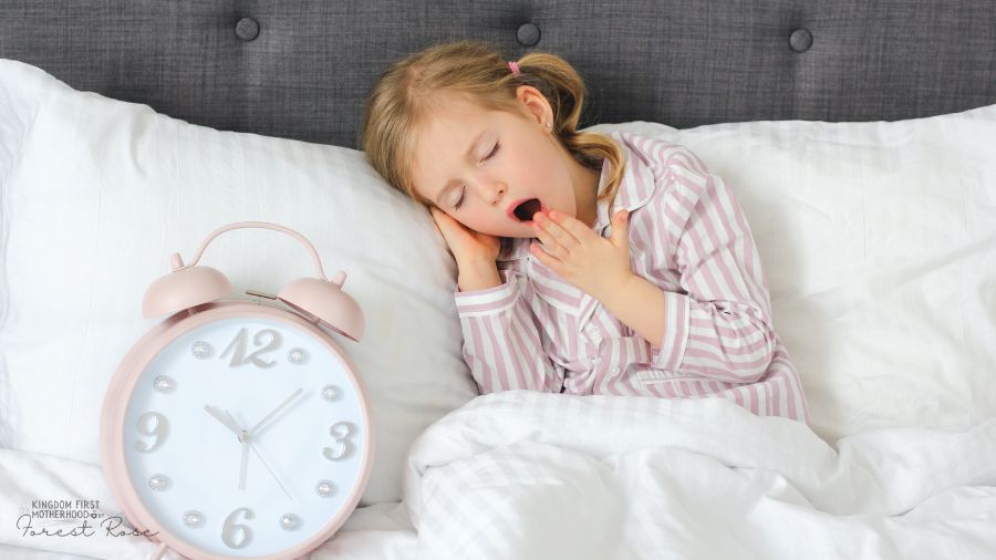 Little girl yawning by a big clock in bed